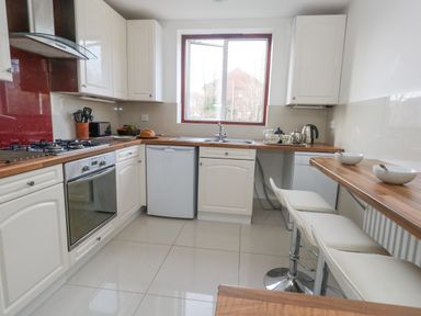 A kitchen with white cabinets wooden countertops a window a stove oven a dishwasher a refrigerator a sink and white bar stools at Kiama in Weymouth
