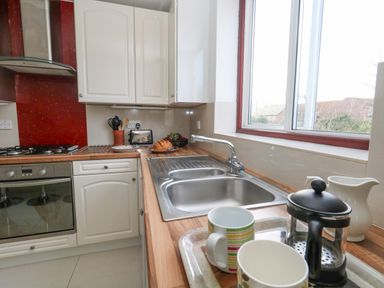 A kitchen with a double sink cups a coffee press bread and fruit on the counter at Kiama in Weymouth