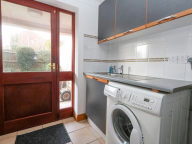 A laundry room with a washing machine sink and cupboards next to a wooden door with glass panels at Kiama in Weymouth
