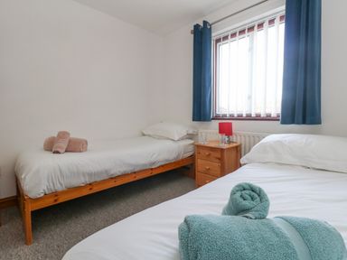 A bedroom with two single beds with towels on them a wooden bedside table with a lamp and a window with blue curtains at Kiama in Weymouth