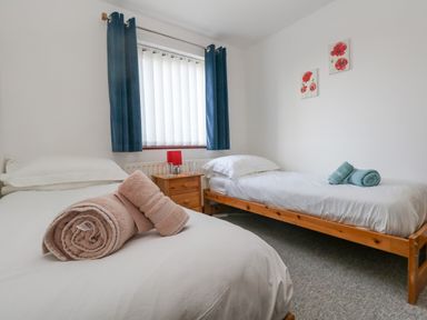 A bedroom with two single beds with folded towels on them a wooden nightstand with glasses and a lamp and blue curtains at Kiama in Weymouth