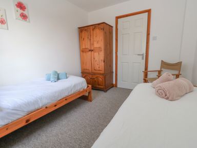 A bedroom with two single beds with rolled towels a wooden wardrobe a light grey door and a wooden chair at Kiama Weymouth