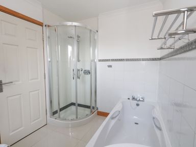 A bathroom with a shower enclosure and a bathtub with grab bars at Kiama in Weymouth