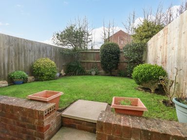 A small fenced garden with green grass shrubs and flower pots at Kiama in Weymouth