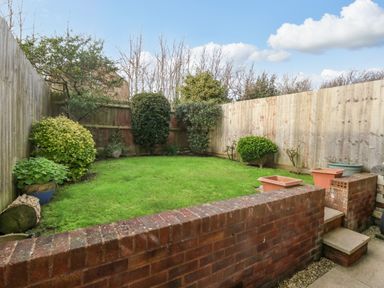 A small garden with grass and bushes surrounded by wooden fences and a brick wall with steps at Kiama in Weymouth