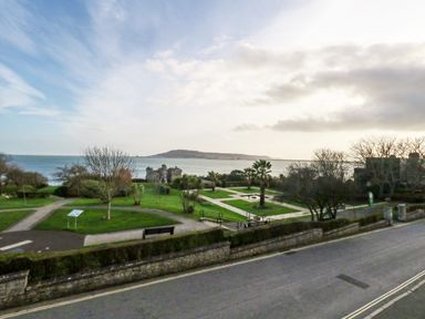 A seaside park with pathways benches palm trees and a distant island visible across the water at Kiama Weymouth