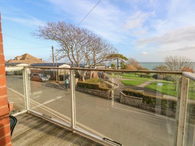 A balcony with glass railing overlooking a street park with trees and ocean in the background at Kiama in Weymouth
