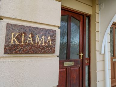 A close up of a brown wooden door with frosted glass panels and a brass mail slot with the number 84 beside it and a marble plaque with gold letters reading KIAMA