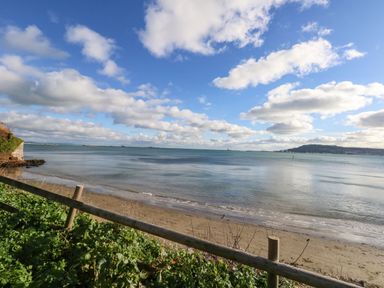 A sandy beach with a wooden railing and vegetation overlooking a calm sea with a hill in the distance