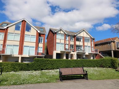 A bench on grassy area in front of residential buildings with balconies and parked cars at Kiama in Weymouth