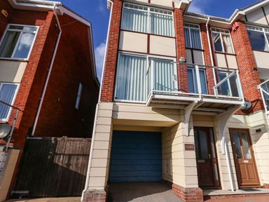 A three story brick house with a blue garage door a balcony and a wooden front door at Kiama in Weymouth