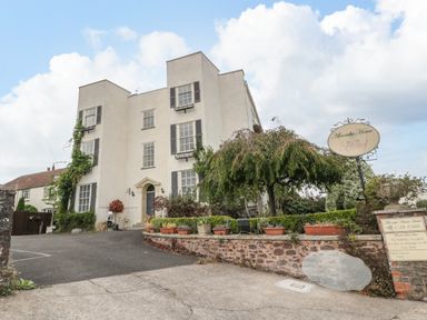 An exterior view of a multi-story building with plants and a driveway at Alcombe House in Minehead