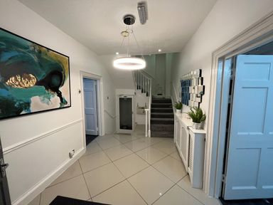 A hallway with stairs a circular ceiling light and plants on a radiator cover at Alcombe House in Minehead