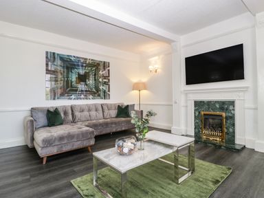 A living room with a gray sofa green rug and a fireplace with a TV above at Alcombe House in Minehead