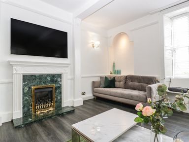 A living room with a gray sofa a marble coffee table a fireplace with a mounted TV and flowers on the table at Alcombe House Minehead