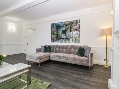 A living room with a sectional sofa gray cushions floor lamp and abstract wall art at Alcombe House Minehead