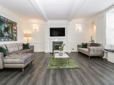 A living room with two sofas a green rug and a wall-mounted TV at Alcombe House Minehead