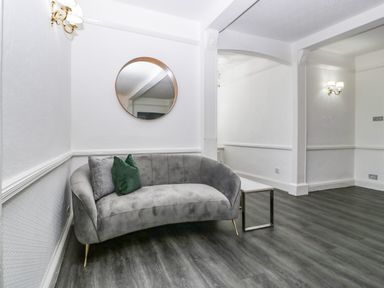A living room with a curved gray sofa green and gray cushions a round wall mirror and a small side table at Alcombe House in Minehead