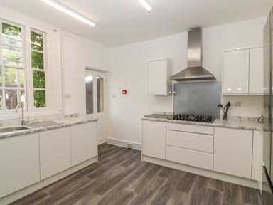 A kitchen with white cabinets marble countertops a gas stove a stainless steel range hood and a window at Alcombe House Minehead