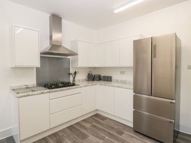 A kitchen with white cabinets marble countertops a stainless steel refrigerator and a gas stove with a vent hood at Alcombe House Minehead