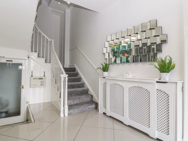 Hallway with a staircase carpeted stairs a radiator cover with plants and a decorative mirror at Alcombe House Minehead