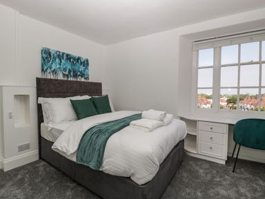 A bedroom with a double bed green pillows a greenthrow a desk and a chair by the window at Alcombe House in Minehead
