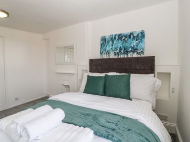 A bedroom with a bed with green cushions and a teal throw with a painting above the bed at Alcombe House in Minehead