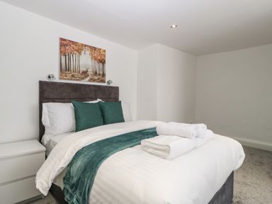 A bedroom with a bed with green pillows and blanket a bedside table and a painting on the wall at Alcombe House in Minehead