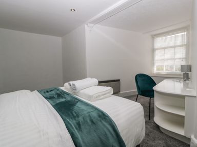 A bedroom with a bed with white linens and teal throw a teal chair and a white desk with shelves at Alcombe House Minehead