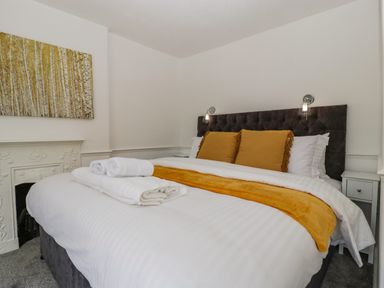 A bedroom with a bed with white linens yellow pillows and blanket and a painting above a fireplace at Alcombe House in Minehead
