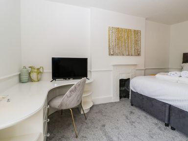 A bedroom with a bed, a desk with a chair, a television, vases, a fireplace, and a painting at Alcombe House Minehead