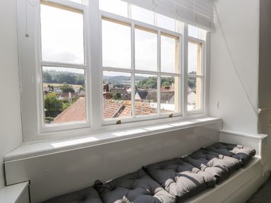 A window seat with cushions and a view of rooftops and hills at Alcombe House in Minehead