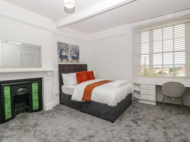 A bedroom with a double bed cushions and blanket a fireplace with green tiles a desk and chair at Alcombe House Minehead