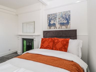 A bedroom with a bed featuring orange pillows and blanket a fireplace with green tiles and two deer paintings above the bed at Alcombe House in Minehead