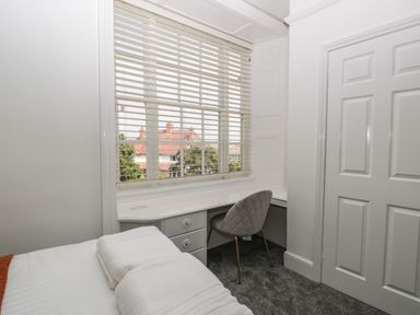A bedroom corner with a desk, a chair, a window with blinds, and a bed with folded towels at Alcombe House in Minehead