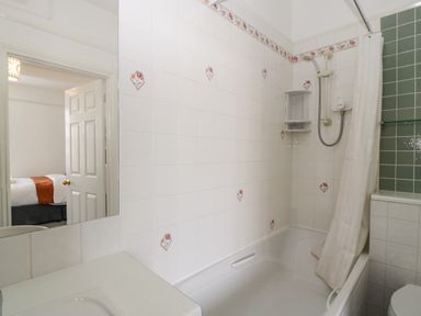 A bathroom with a bathtub shower and tiled walls with floral patterns at Alcombe House in Minehead