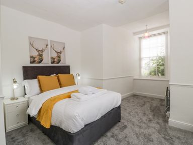 A bedroom with a bed yellow pillows bedside tables lamps and a window with blinds at Alcombe House in Minehead