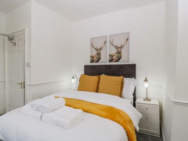 A bedroom with a bed white linens yellow pillows and blanket bedside table with lamp and wall art of deer at Alcombe House Minehead