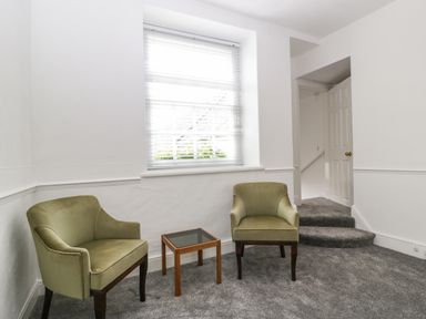 A room with two green armchairs and a small wooden table near a window with blinds at Alcombe House Minehead