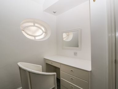 A small workspace with a white desk, drawers, a chair, and an oval window at Alcombe House in Minehead