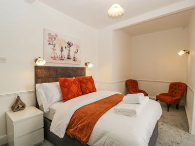 A bedroom with a bed with orange pillows and throw and two orange chairs in a corner at Alcombe House Minehead