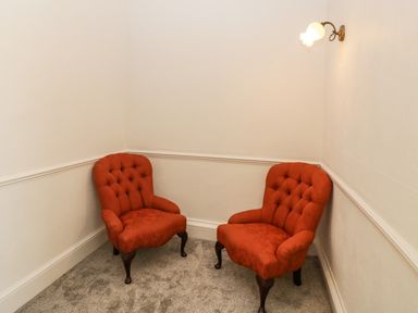 Two red upholstered armchairs on carpeted floor in a corner with white walls and a wall light at Alcombe House in Minehead