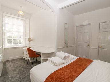 A bedroom with a bed with towels and orange runner a desk with an orange chair and a lamp at Alcombe House in Minehead