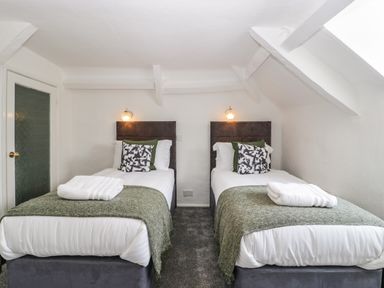 A bedroom with two single beds with patterned pillows and folded towels at Alcombe House Minehead