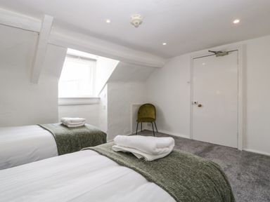 A bedroom with two single beds green throws folded towels an olive green chair and a window at Alcombe House Minehead