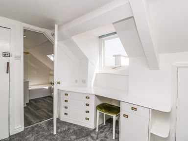 A room with a built-in desk and a green upholstered chair next to a window and an open door leading to a bathroom at Alcombe House Minehead