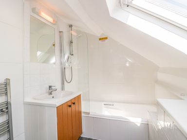 A bathroom with a sink and cabinet a bathtub with shower and skylight window at Alcombe House Minehead