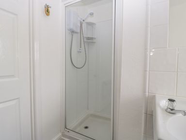 A shower enclosure with glass door and a white electric shower unit in a bathroom at Alcombe House in Minehead
