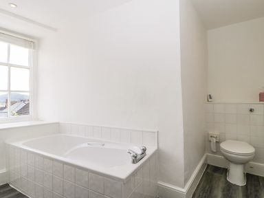 A bathroom with a bathtub under a window and a toilet next to a half tiled wall at Alcombe House in Minehead