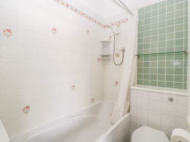 A bathroom with a bathtub and shower with floral tiles at Alcombe House in Minehead